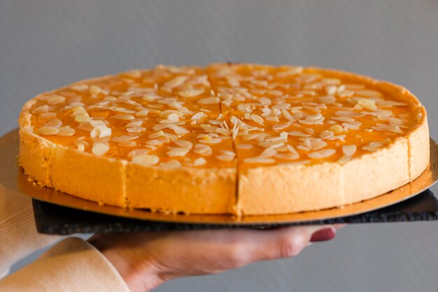 Cheesecake all'olivello spinoso cosparsa di petali di mandorle? con una tazza di tè alla frutta in un'accogliente caffetteria, sfondo scuro