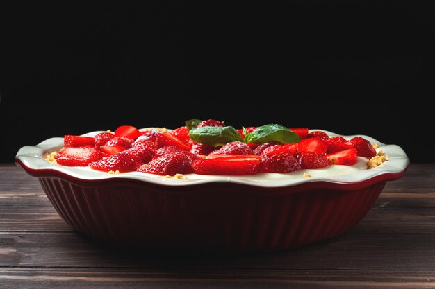 Cheesecake alla fragola con foglie di basilico, in una teglia in ceramica rossa su un tavolo di legno