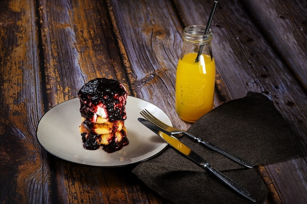 Cheesecake con marmellata di mirtilli e panna acida su un piatto con succo d'arancia in bottiglia