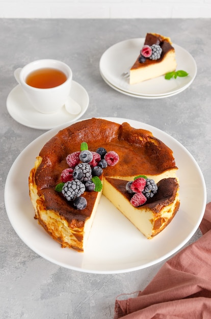 Cheesecake di San Sebastian con frutti di bosco e foglie di menta in cima su un piatto bianco su uno sfondo grigio cemento. Dolce spagnolo tradizionale. Copia spazio.