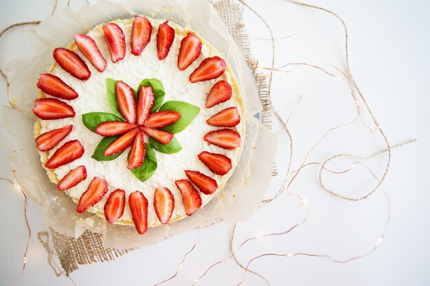 Cheesecake estiva molto bella decorata con fragole - si erge su un tavolo di legno bianco, vista dall'alto