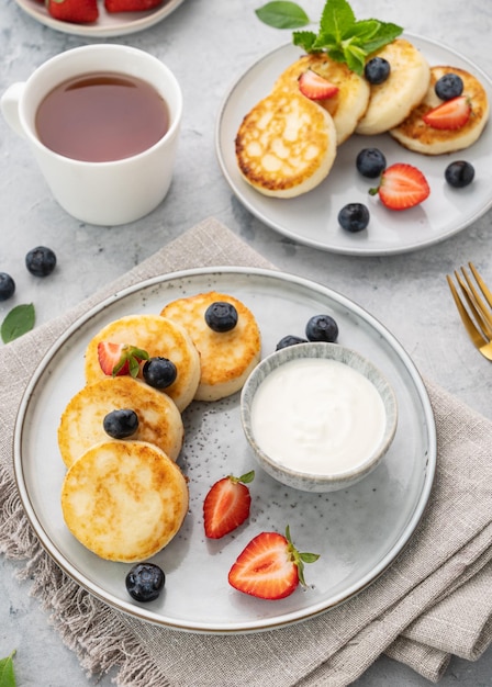 Cheesecake o ricotta o syrniki con blerries freschi e panna acida su sfondo grigio con una tazza di tè Il concetto di una colazione sana e deliziosa Orientamento verticale