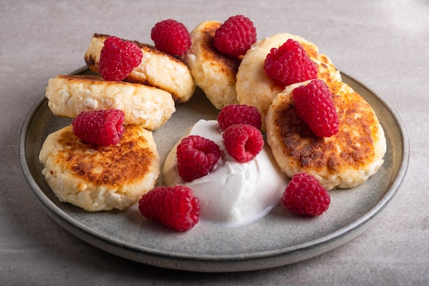 Cheesecake o syrniki su un piatto rotondo con lampone, panna acida e sciroppo di lampone.