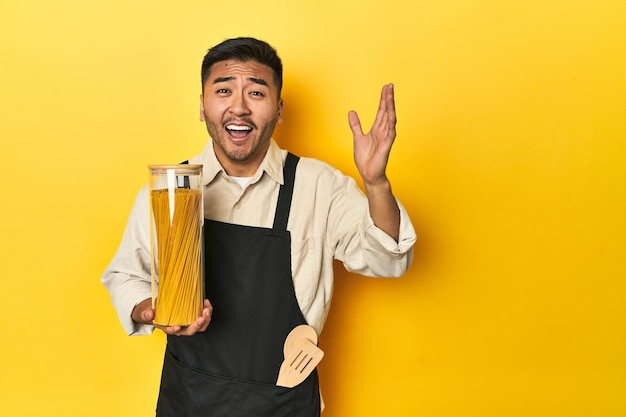 Chef asiatico con barattolo di spaghetti che riceve una piacevole sorpresa eccitato e alzando le mani