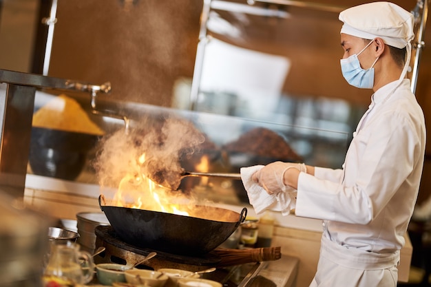 Chef asiatico professionista che fa soffriggere nel wok fiammeggiante