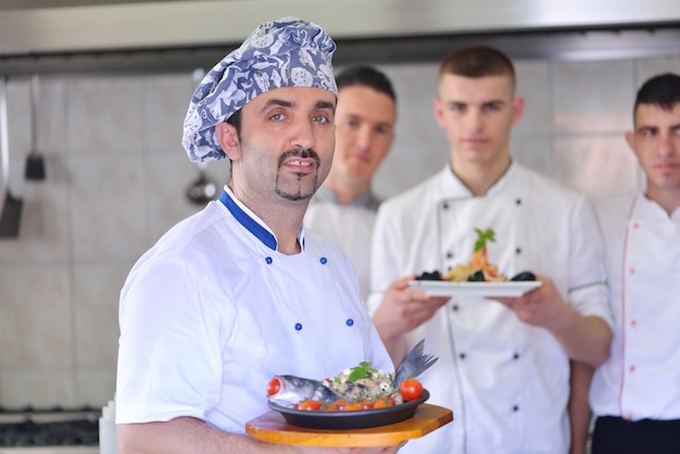 Chef bello vestito in uniforme bianca che decora insalata di pasta e pesce di mare in una cucina moderna