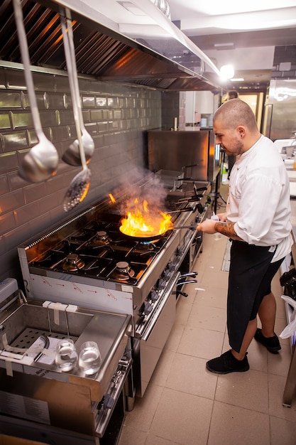 Chef che cucina e fa flambe sul cibo nella cucina del ristorante, ottimo cuoco al lavoro