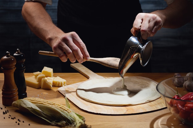 Chef che cucina la pizza, mettendo la salsa bianca sulla base della pizza