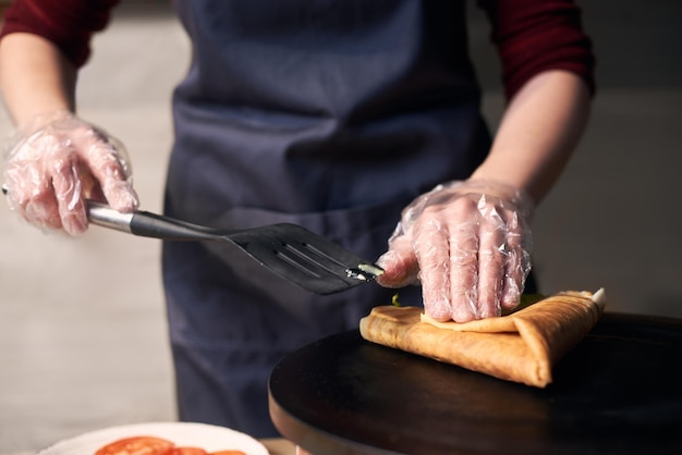 Chef che prepara crepe ripiene arrotolare crepe sul piano cottura caldo Concetto di cucina tradizionale ristorante Vista frontale dettagliata