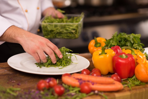 chef che serve insalata di verdure sul piatto nella cucina del ristorante