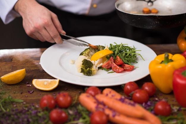 chef che serve insalata di verdure sul piatto nella cucina del ristorante