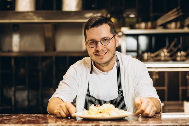 Chef che serve insalata e in piedi accanto al bancone della cucina