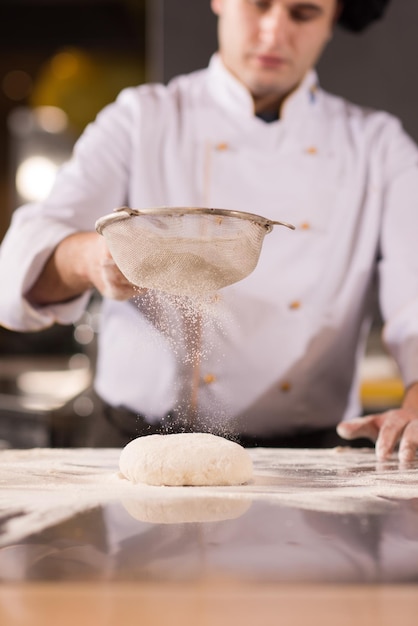 chef che sparge farina sopra l'impasto della pizza fresca sul tavolo della cucina