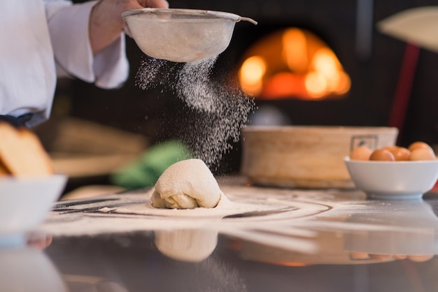 chef che sparge farina sopra l'impasto della pizza fresca sul tavolo della cucina