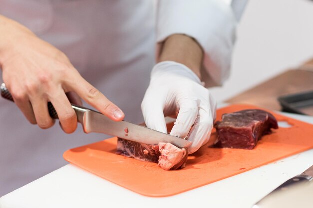 Chef che taglia carne cruda fresca con un coltello in cucina Chef che taglie carne di manzo su una tavola