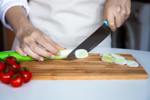 Chef che taglia i porri su una tavola di legno