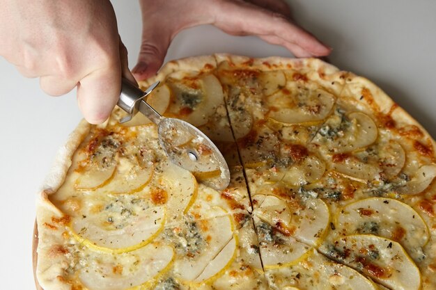 Chef che taglia pizza alla frutta di pera con coltello su tavola di legno su tavolo bianco closeup