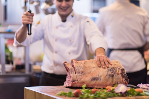 chef che usa l'ascia mentre taglia un grosso pezzo di manzo su una tavola di legno nella cucina del ristorante