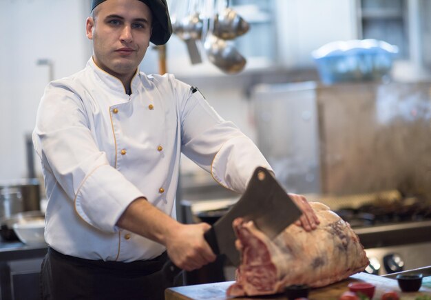 chef che usa l'ascia mentre taglia un grosso pezzo di manzo su una tavola di legno nella cucina del ristorante