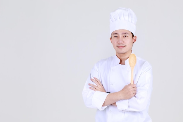 Chef cinese esperto e intelligente su un elegante sorriso uniforme da cucina e in piedi con sicurezza in cucina con il braccio incrociato e il cucchiaio come esperto qualificato di cucina per cene di lusso al ristorante.