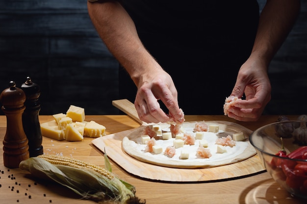 Chef di cucina pizza, mettendo la guarnizione sulla base della pizza