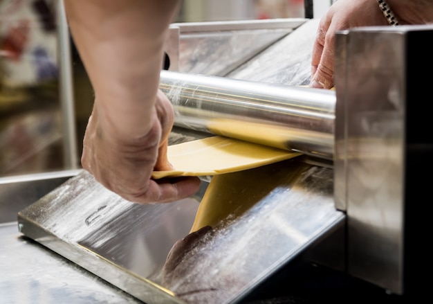 Chef di laminazione della pasta con una macchina per pasta. Macchina per pasta.