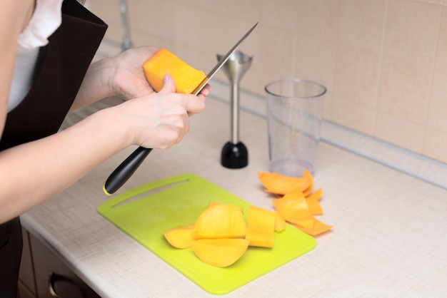 Chef donna che taglia mango fresco per preparare un gustoso frullato o succo di mango fatto in casa Focus selettivo Processo di preparazione di bevande estive a casa stile di vita sano