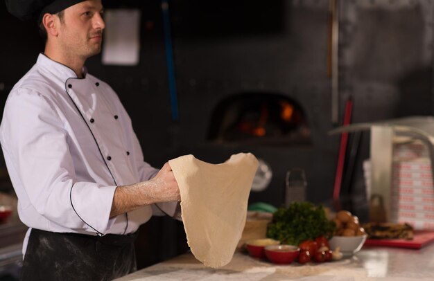 Chef esperto che prepara l'impasto per la pizza arrotolando con le mani e vomitando