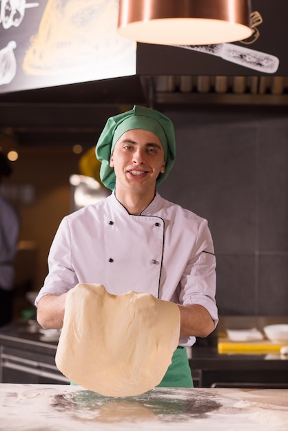 Chef esperto che prepara l'impasto per la pizza arrotolando con le mani e vomitando