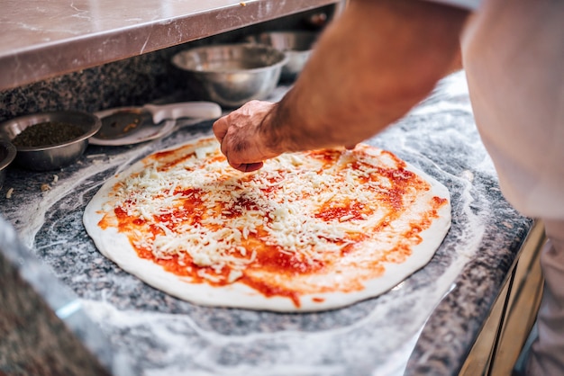 Chef facendo la pizza. Avvicinamento. Aggiunta di formaggio su base di pizza.