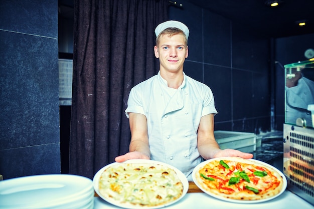 Chef fornaio cuoco in uniforme nera che mette la pizza nel forno con la pala nella cucina del ristorante.