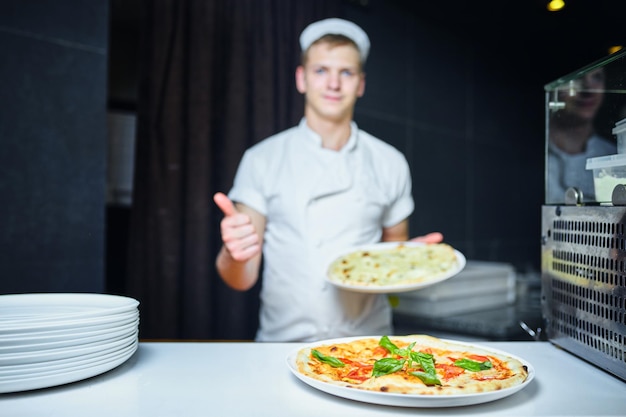 Chef fornaio cuoco in uniforme nera che mette la pizza nel forno con la pala nella cucina del ristorante.