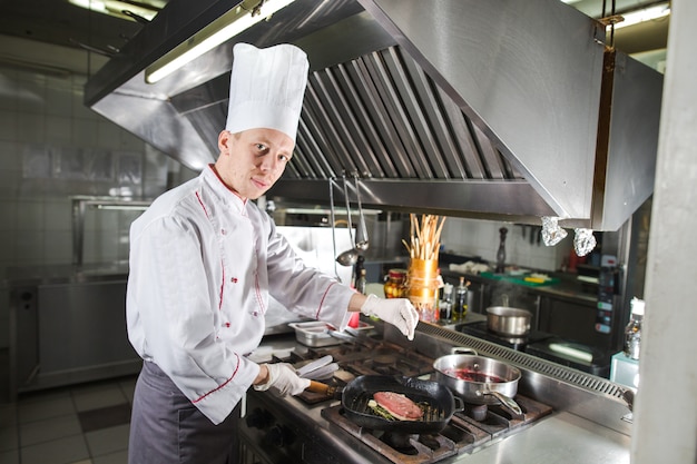 Chef in cucina del ristorante a piano cottura con padella, cottura