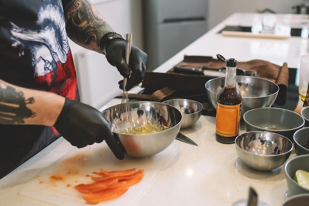 Chef in guanti di gomma neri che monta la salsa con una frusta