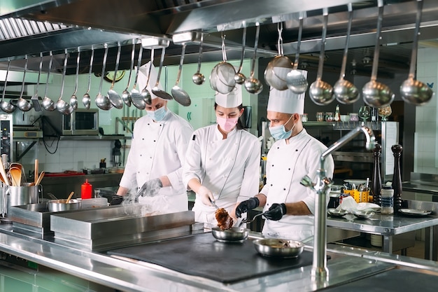 Chef in guanti e maschere protettive preparano il cibo nella cucina di un ristorante o di un hotel.