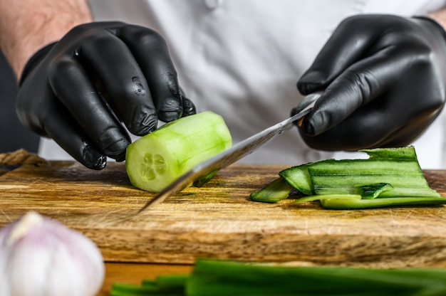 Chef in guanti neri che affetta un cetriolo