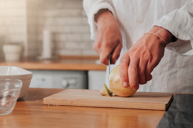 Chef irriconoscibile che taglia la cipolla su una tavola di legno