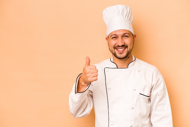 Chef ispanico uomo isolato su sfondo beige sorridente e alzando il pollice