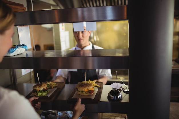 Chef passando vassoio con patatine fritte e hamburger alla cameriera