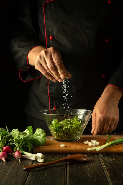 Chef professionista aggiunge sale a un'insalata di lattuga fresca Cucina cibo vegetariano in cucina Menu per un ristorante o un hotel