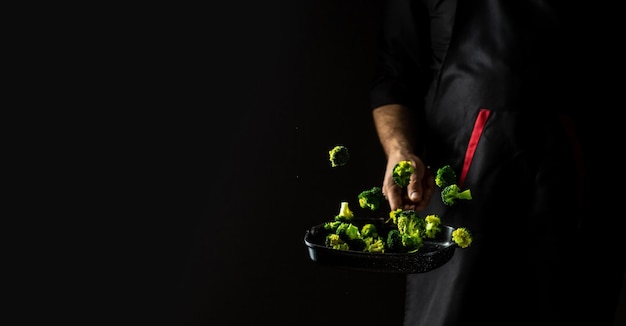 Chef professionista cuochi Flambe Style Mani di cuoco che friggono le verdure su verdure volanti in padella che si spargono in un movimento di congelamento