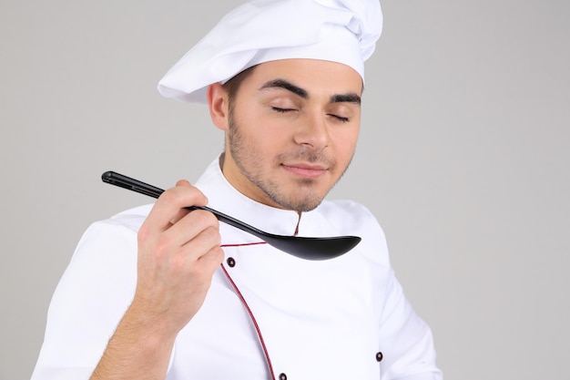 Chef professionista in uniforme bianca e cappello su sfondo grigio