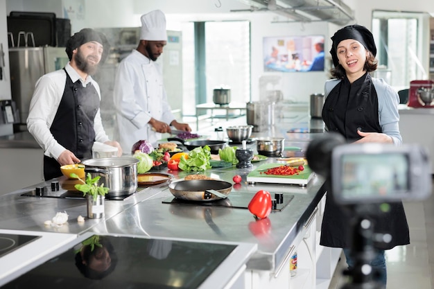 Chef sorridenti felici che girano video culinari nella cucina del ristorante mentre preparano un piatto delizioso. Cuochi multietnici che registrano il processo di preparazione del cibo per i programmi di cucina televisiva.