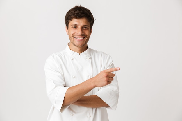 Chef uomo in piedi isolato sul muro bianco che punta a copyspace.