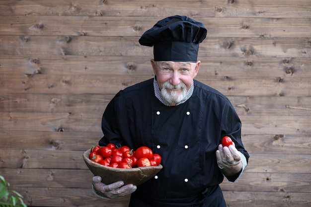 Chef vecchio in uniforme con verdure fresche su un bacground di legno