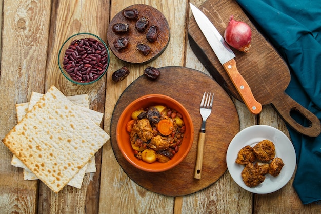 Chelnt piatto ebraico con carne in un piatto su un tavolo di legno su un supporto accanto a un coltello e ingredienti. Foto orizzontale