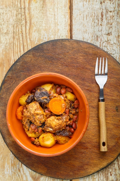 Chelnt piatto ebraico con carne sul tavolo in un piatto su un supporto di legno rotondo.