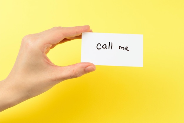 Chiamami testo su una carta in mano di donna su sfondo giallo