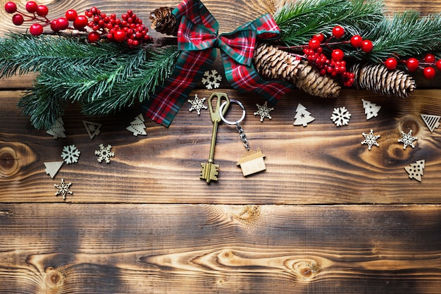 Chiave di casa con cottage portachiavi su uno sfondo festoso ecologico e naturale con albero di Natale. Felice Anno Nuovo-sfondo rosso, regalo, biglietto di auguri. Acquisto, costruzione, trasferimento, mutuo