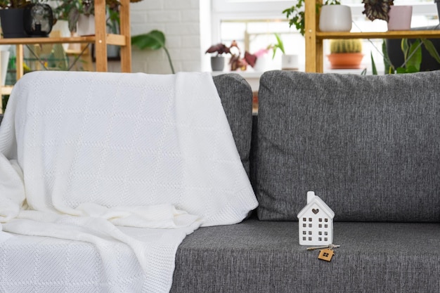 Chiave di casa con portachiavi e miniatura di casa sul divano grigio con interni bianchi con piante in vaso Progetto di design trasloco in una nuova casa mutuo affitto e acquisto immobile